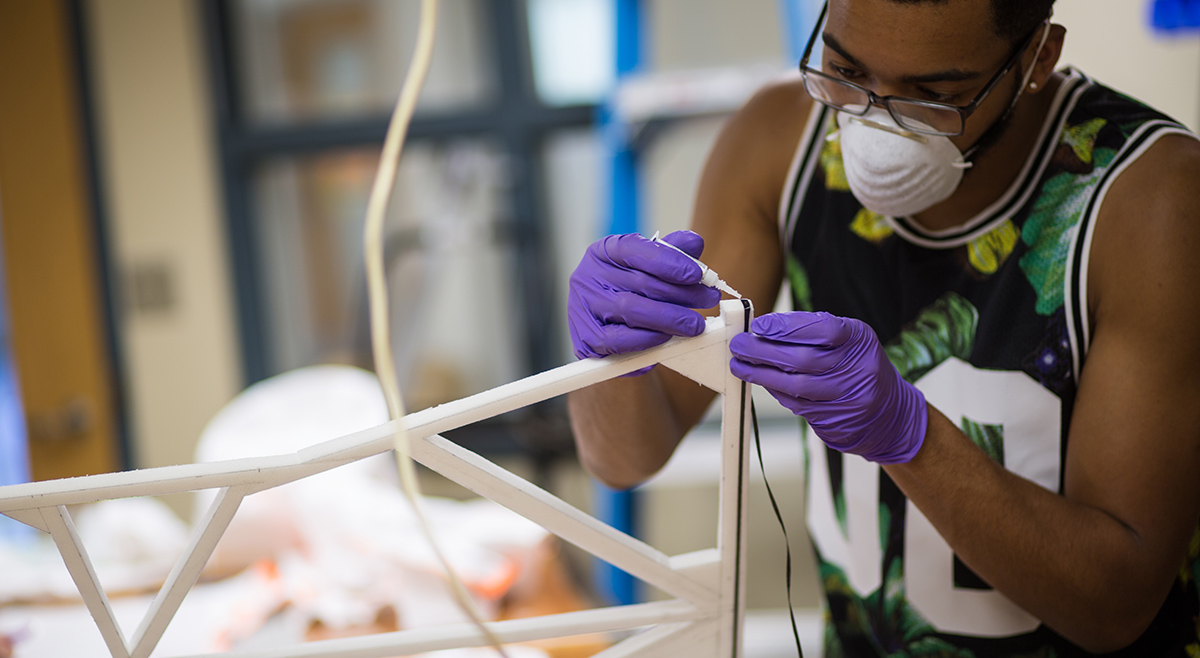 A man from the JHU Mechanical Engineering department adheres an item to a structure as part of a project for the Whiting School of Engineering's Design Day.